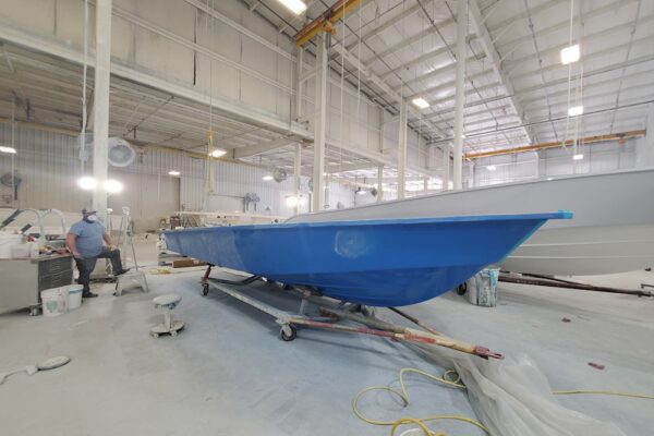 A blue Everglades boat under construction in an industrial warehouse with workers