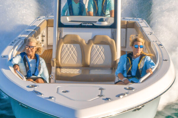 An Everglades boat in motion on water with two people in life jackets sitting at the bow