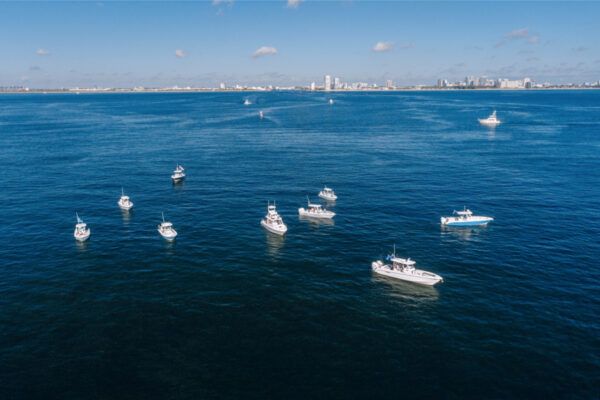 DJI_0521_2909 Aerial view of several Everglades boats floating on calm water with a distant city skyline under a clear blue sky