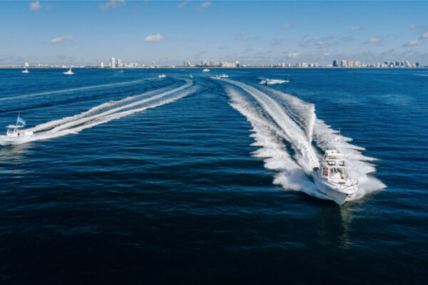 DJI_0525_7372 Multiple Everglades boats speeding through the water leaving wakes behind them with a distant city skyline under a clear blue sky