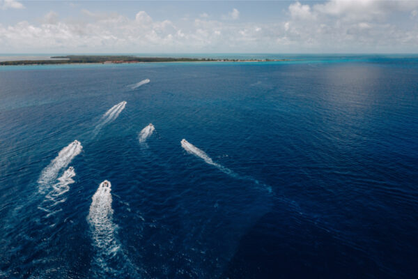 DJI_0554_1668 Aerial view of multiple Everglades boats speeding through the open ocean leaving white wakes behind them with a distant shoreline and cloudy sky in the background