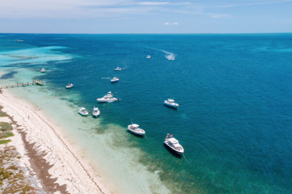 DJI_0673_4843 Aerial view of several Everglades boats anchored near a sandy shoreline with clear blue and turquoise waters stretching into the distance under a sunny sky