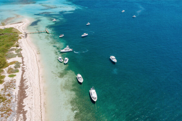 DJI_0675_6626 An aerial view of multiple Everglades boats anchored near a sandy beach with clear blue water surrounding them
