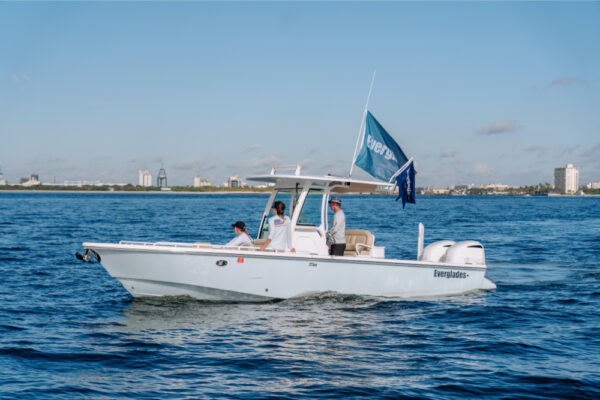 JJS06607_4178 An Everglades boat cruising on calm water with three people on board, flying an Everglades flag, and a city skyline visible in the background