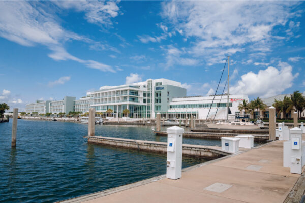 JJS06889_6102 A view of a marina with empty docks and a large modern building in the background under a bright blue sky with scattered clouds