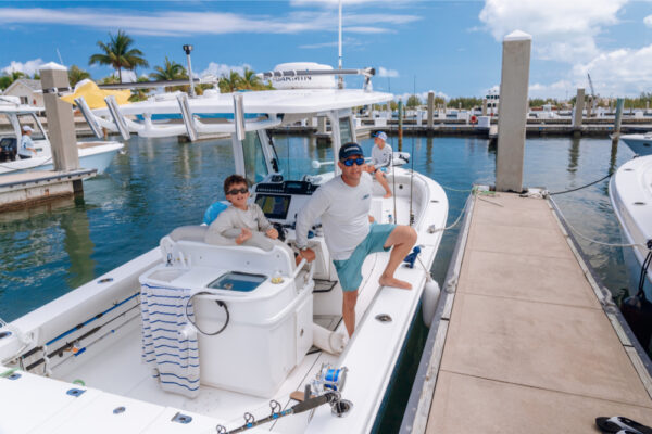 JJS06904_5121 Two people sitting on an Everglades boat docked at a marina on a sunny day with other boats and palm trees in the background