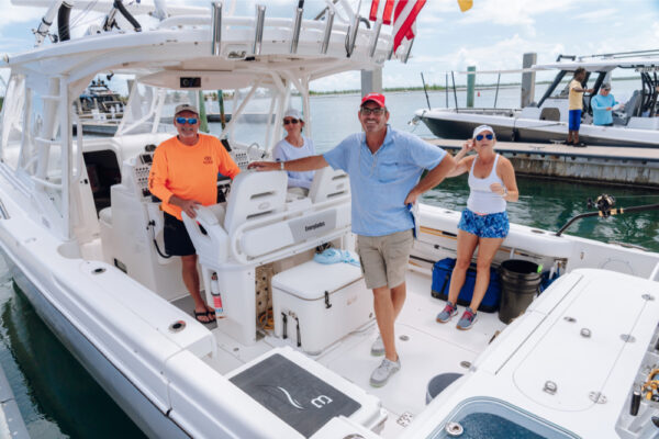 JJS06908_104 Four people standing on an Everglades boat docked at a marina with other boats visible in the background