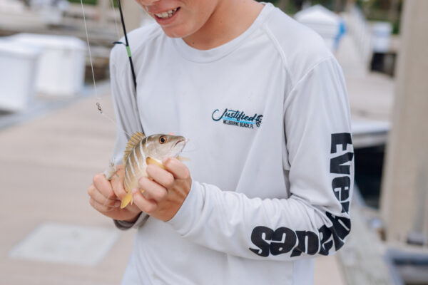 JJS06922_7528 A person holding a small fish they just caught while wearing a long sleeve Everglades shirt at a marina