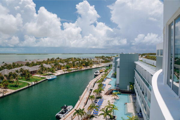 JJS07006_1185 Aerial view of a marina with boats docked along a waterway surrounded by palm trees and buildings with a large hotel and pool area on the right side under a partly cloudy sky