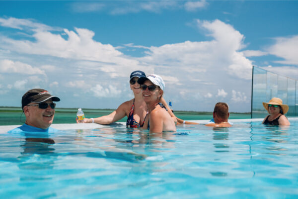 JJS07025_3652 Group of people relaxing in an infinity pool under a sunny sky