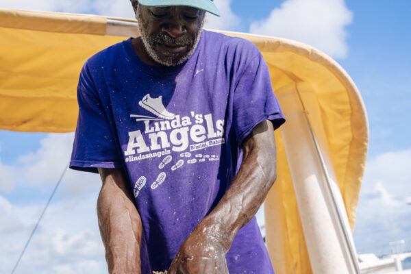 JJS07290_1512 A man wearing a blue hat and a purple shirt working with his hands under a yellow canopy on a sunny day