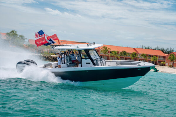 JJS09739_4214 An Everglades boat speeding across turquoise water with multiple flags flying at the back and a shoreline with orange roofed buildings and palm trees in the background