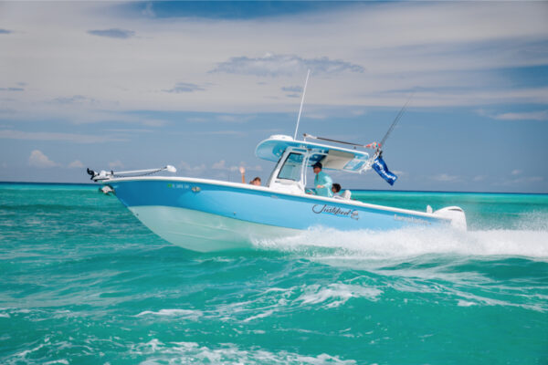 JJS09857_6210 An Everglades boat speeding across turquoise water with fishing rods and flags visible and a partly cloudy sky in the background