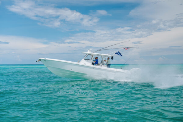 JJS09998_3680 A white boat speeding across turquoise water under a partly cloudy sky, with flags flying from the rear