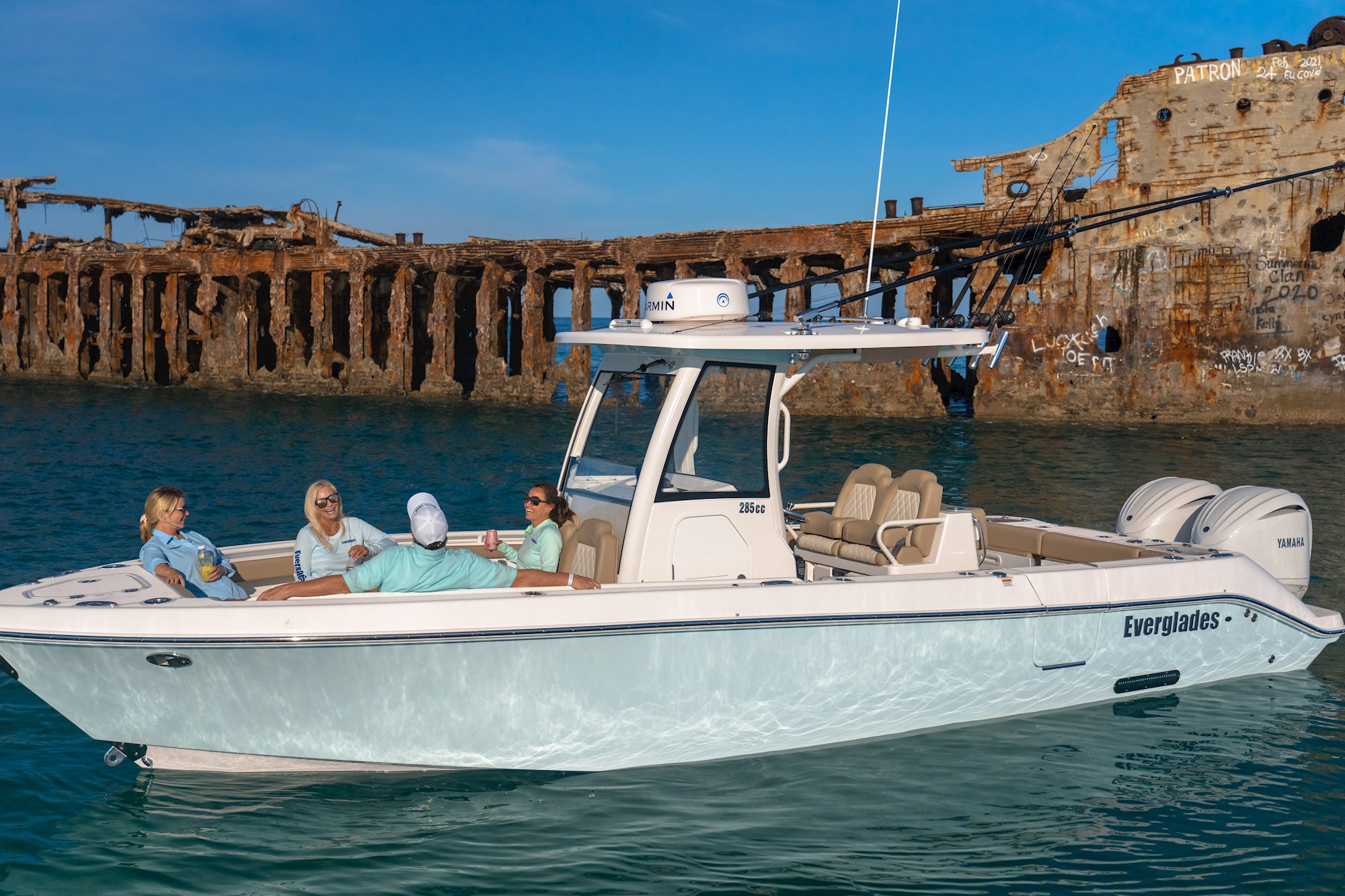 A group of people on a white Everglades Boats near a rusted shipwreck under a clear sky