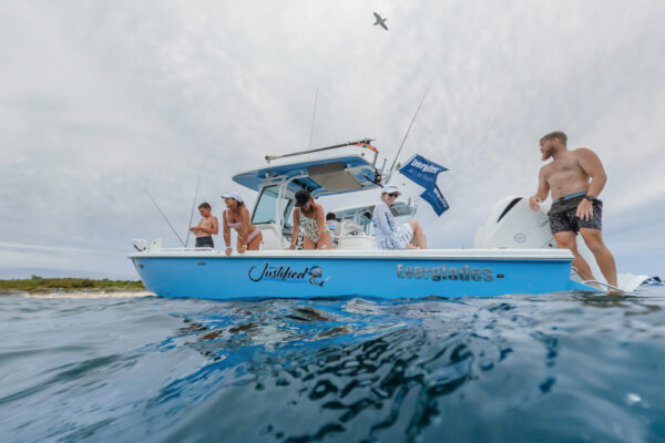 uw8141_7824 An Everglades boat with several people on board enjoying the water, fishing, and relaxing under a cloudy sky with a bird flying overhead